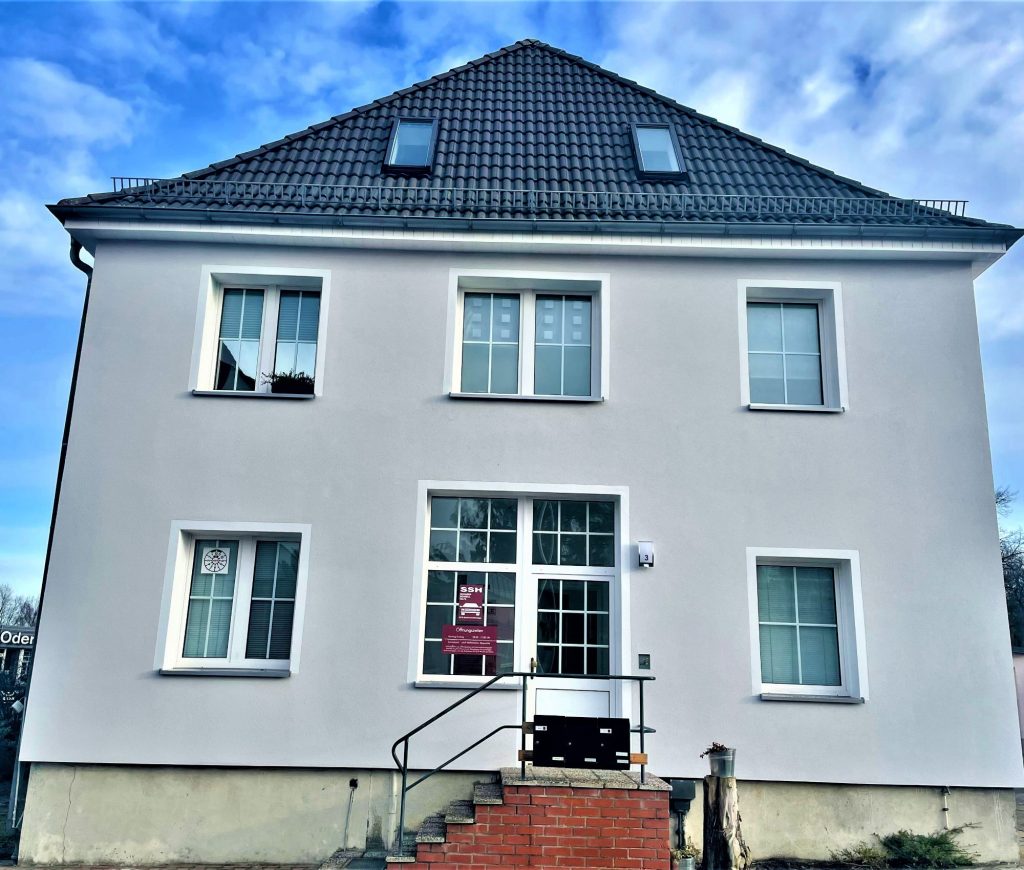 Ein neu renoviertes Gebäude in Angermünde mit einer frisch gestrichenen, sauberen Fassade, das die professionellen Fassadenarbeiten in Angermünde durch Abauservice zeigt. Das weiße Haus mit dunklem Dach und modernen Fenstern steht unter einem klaren blauen Himmel.