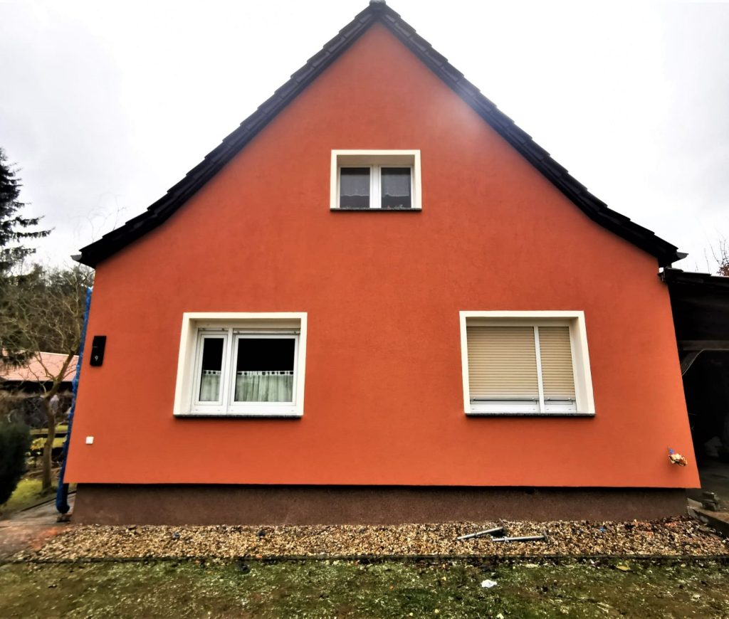 Ein Einfamilienhaus mit frisch renovierter, orangefarbener Fassade, das das Ergebnis professioneller Fassadenarbeiten in Eberswalde durch Abauservice zeigt.